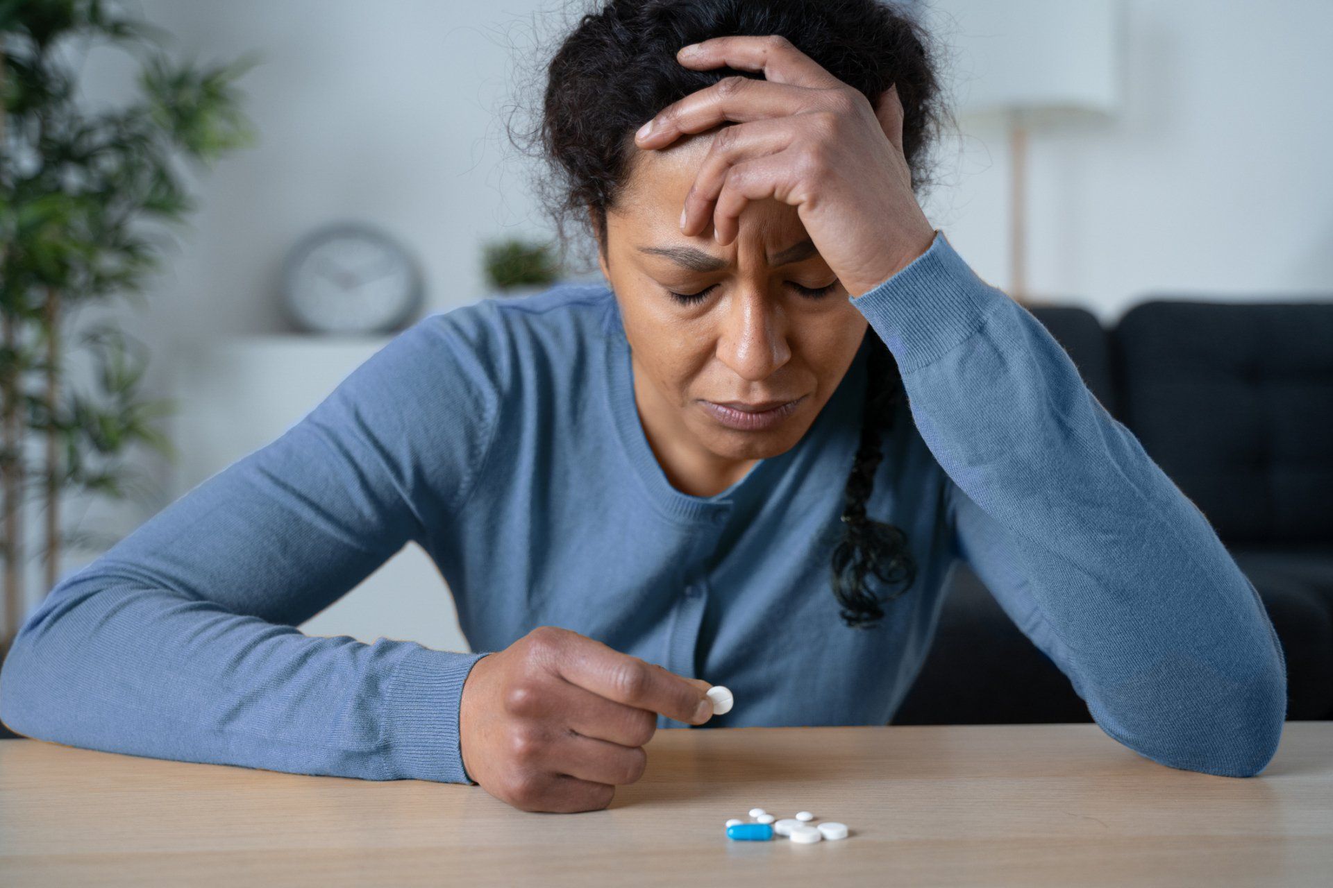 woman on the table holding an antidepressant pill with head on one hand