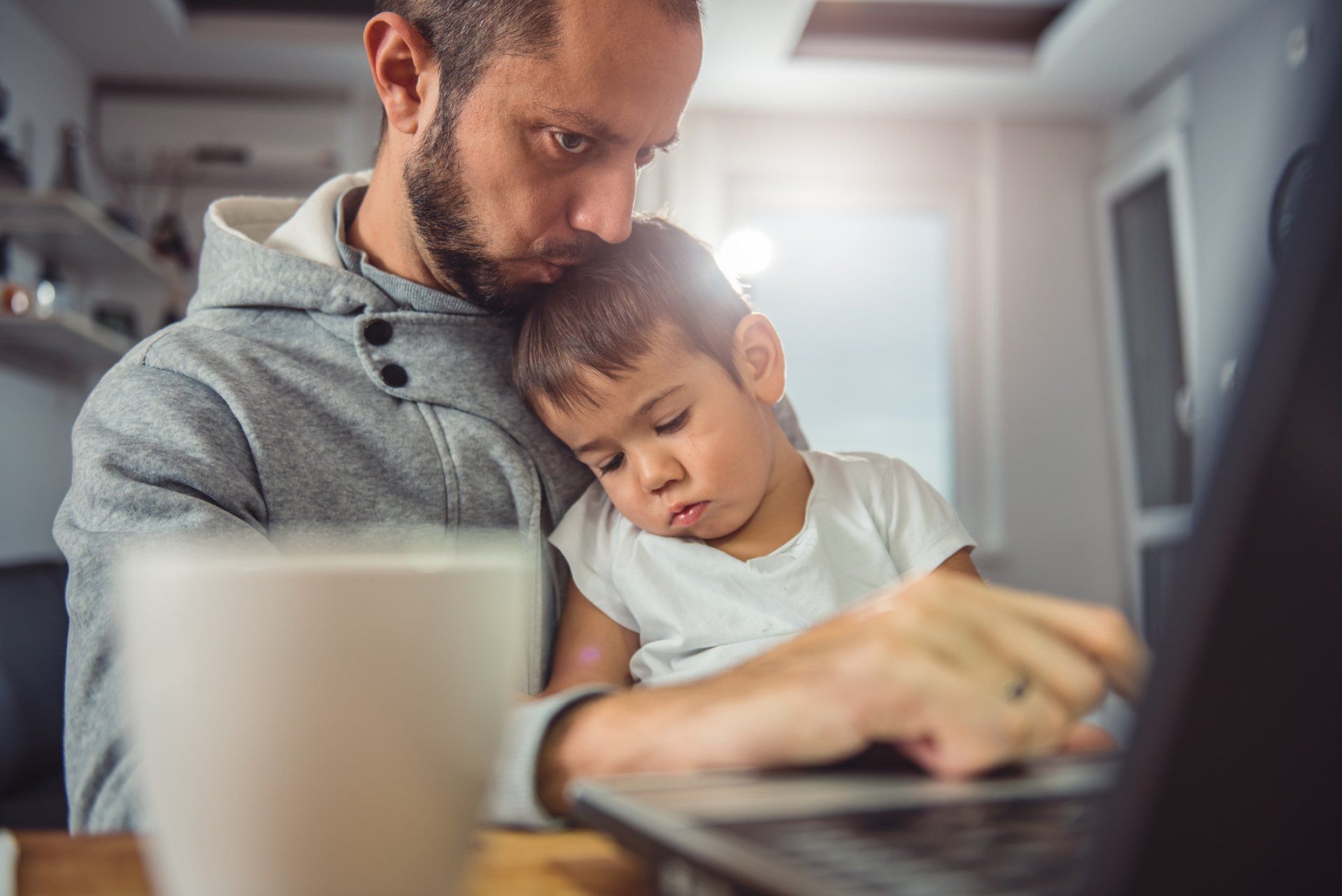 Single father with his son on his lap on the computer making an online appointment to a therapist