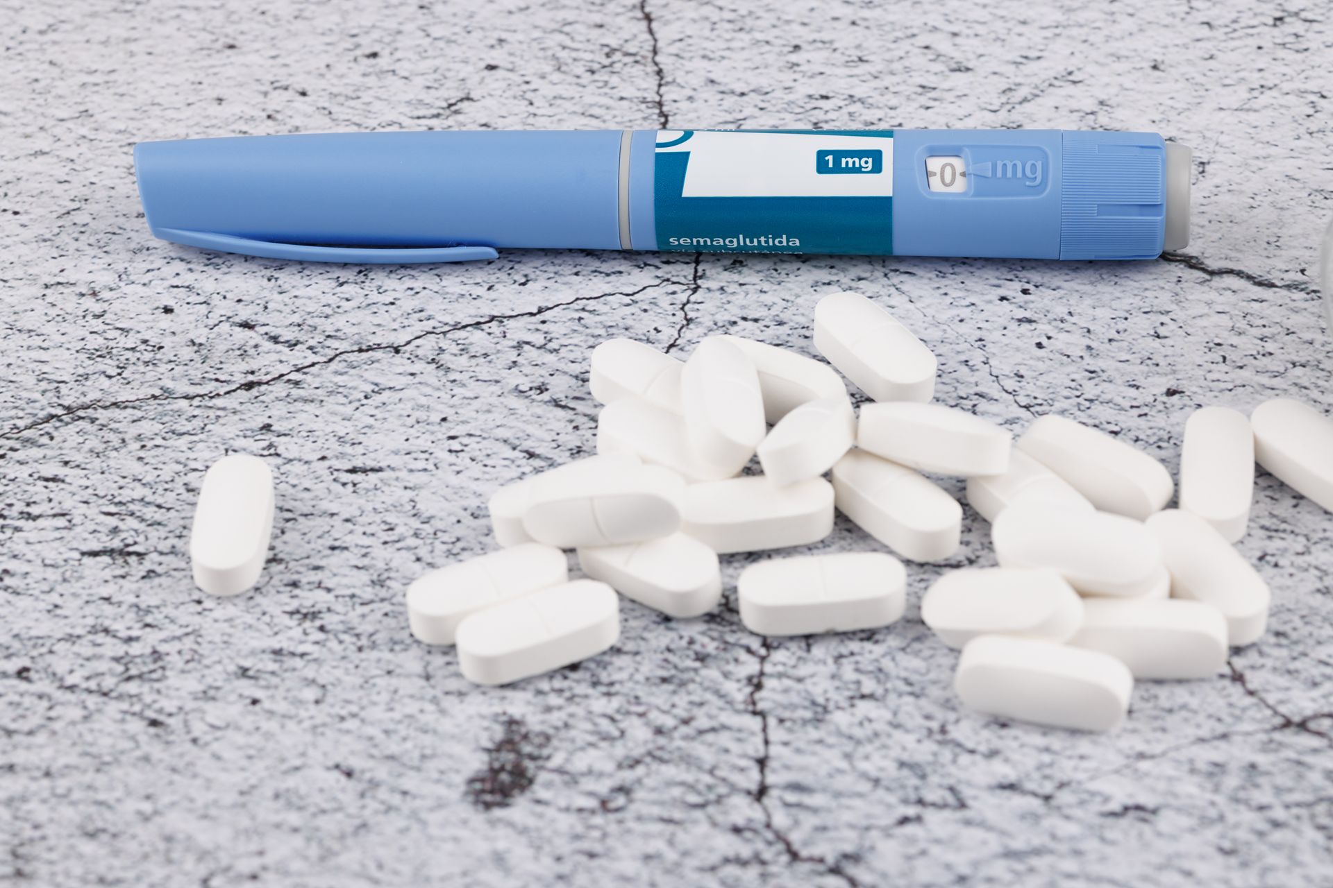 Blue pen-shaped device beside scattered white tablets on a gray surface