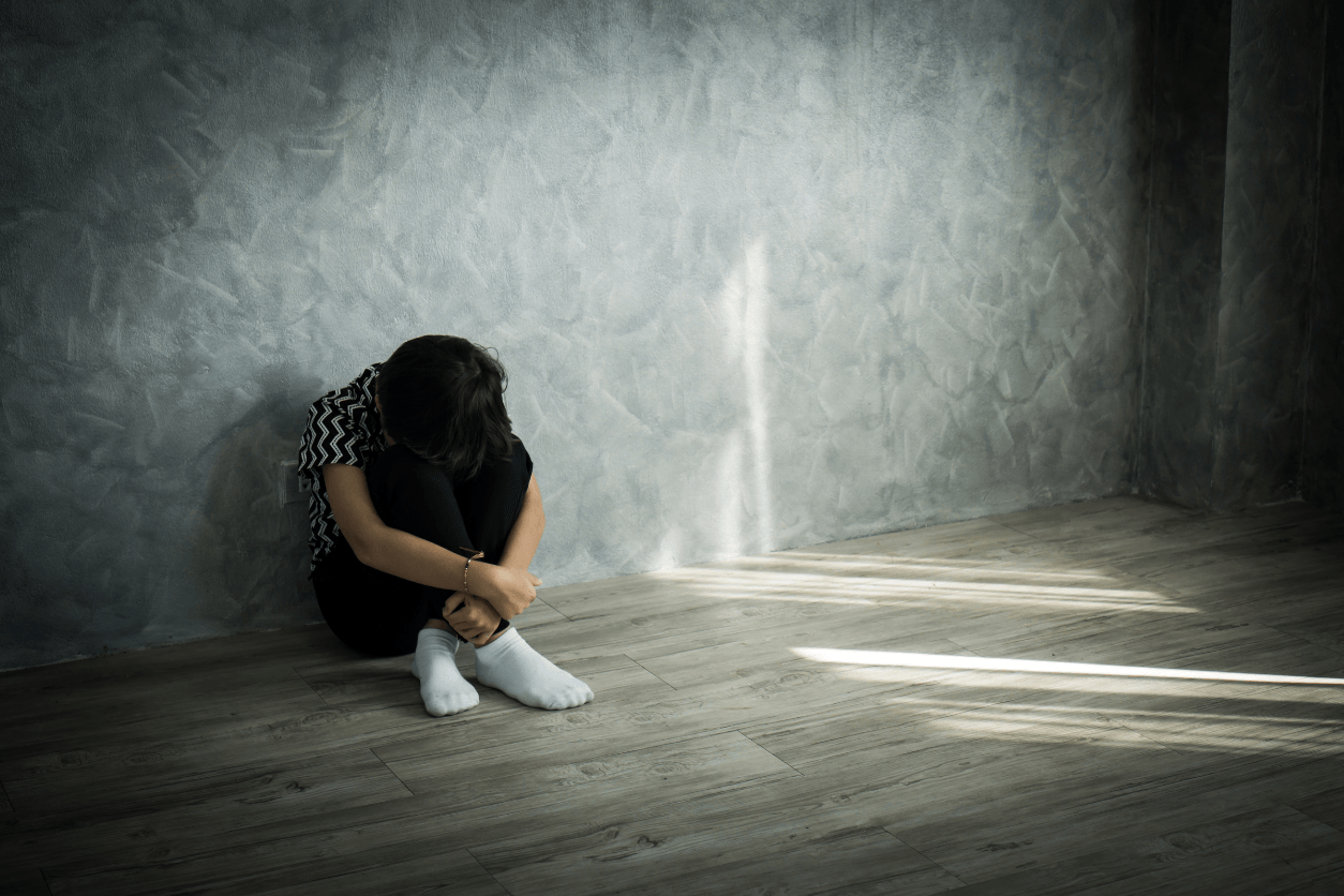 woman sitting on the floor against the wall with her head on both her knees suffering with mental issues