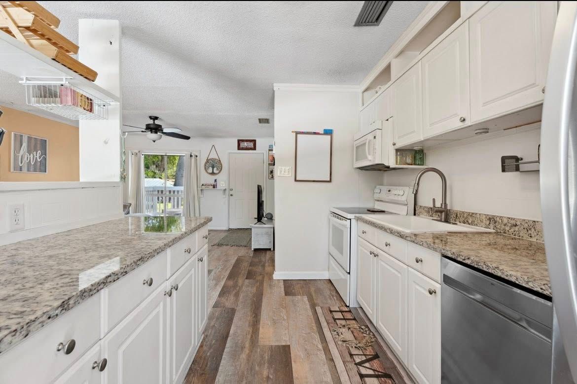 Kitchen with white cabinets, granite countertops, and stainless steel appliances; wood floor.