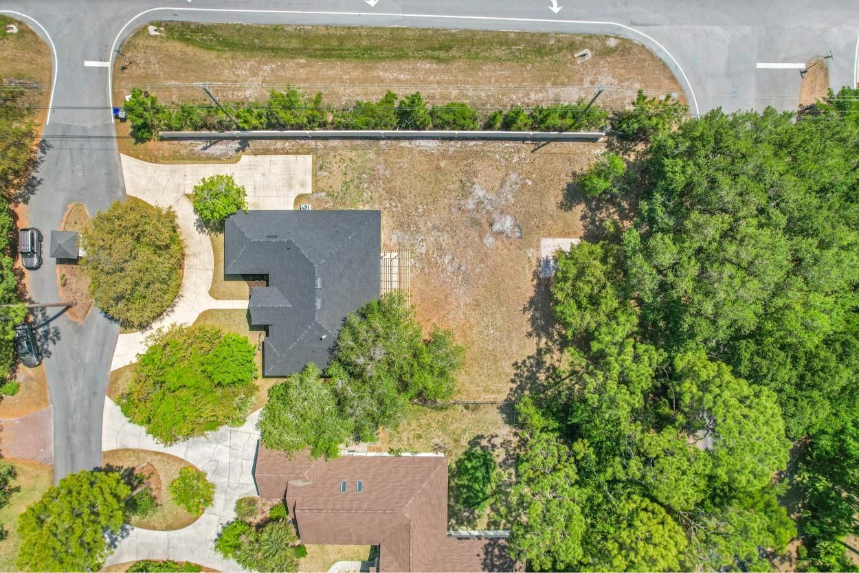 Aerial view of a house with trees, driveway, and road beside it