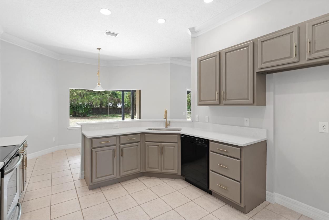 Bright modern kitchen with gray cabinets, white countertops, tile floor, and a window over the sink.