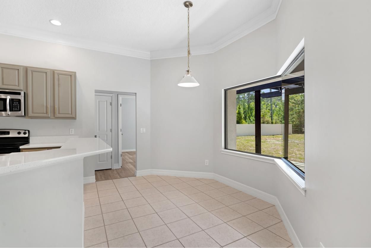Empty modern kitchen with light gray walls, tile floor, white counters, and a large window overlooking greenery