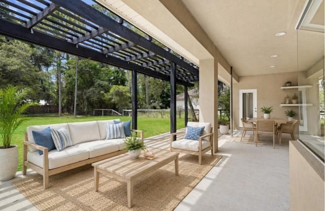 Modern covered patio with outdoor sofa, lounge chairs, and dining area overlooking a green garden