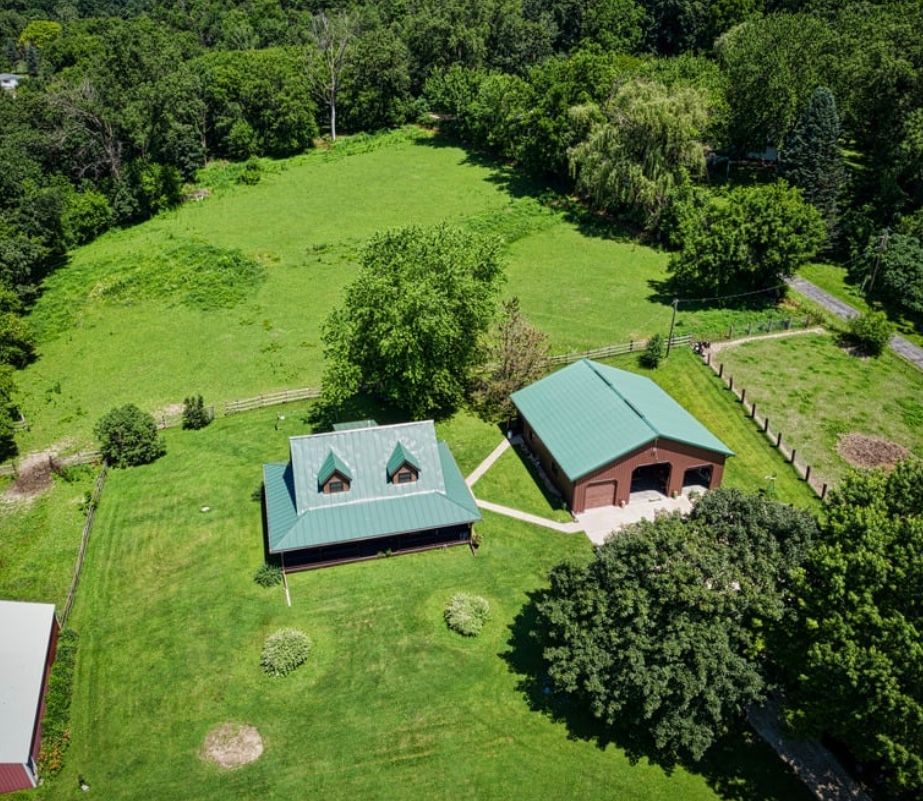 Aerial view of two green-roofed cabins beside a grassy clearing and dense forest