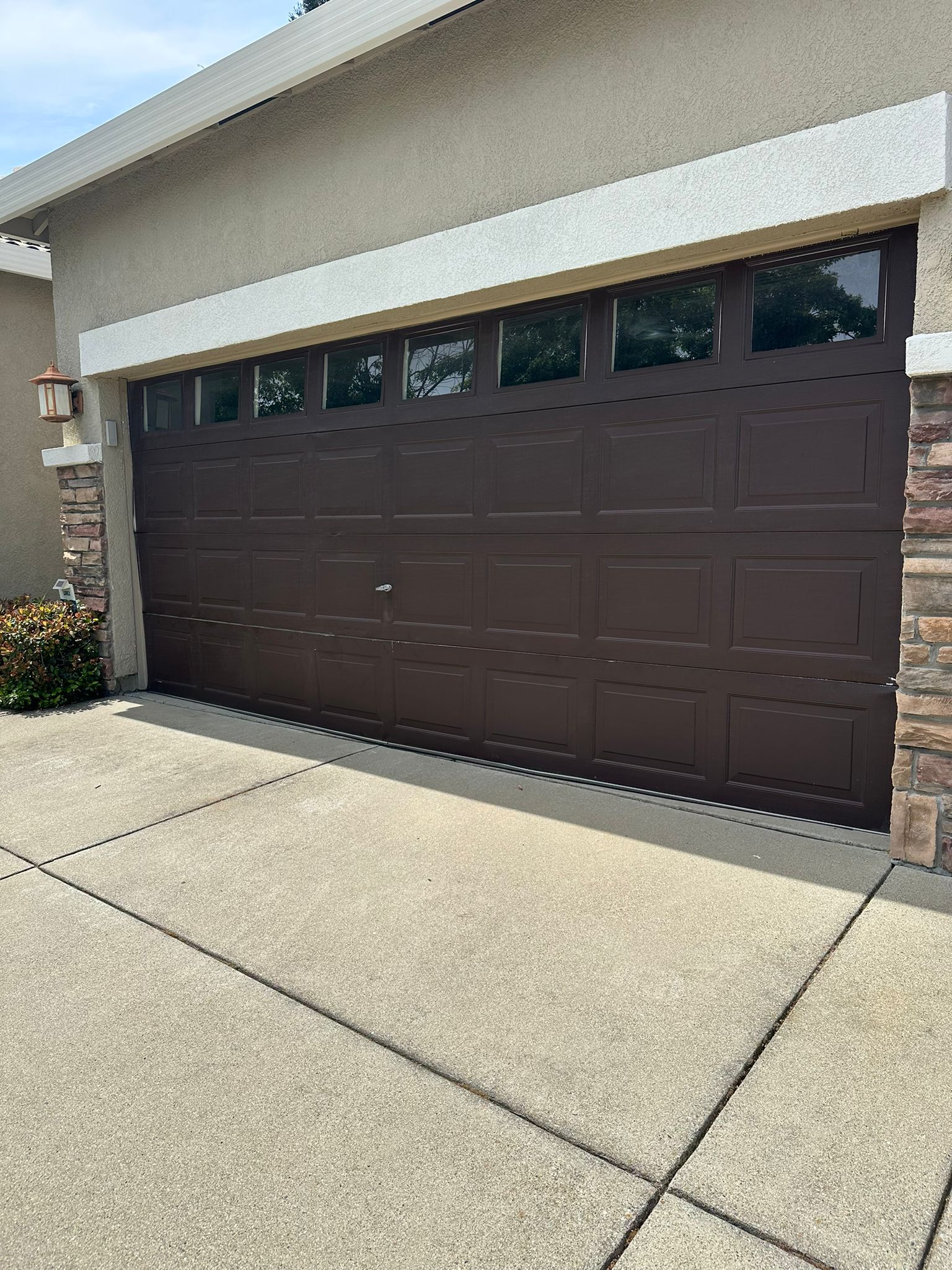 Brown garage door with small windows on a beige house exterior and concrete driveway