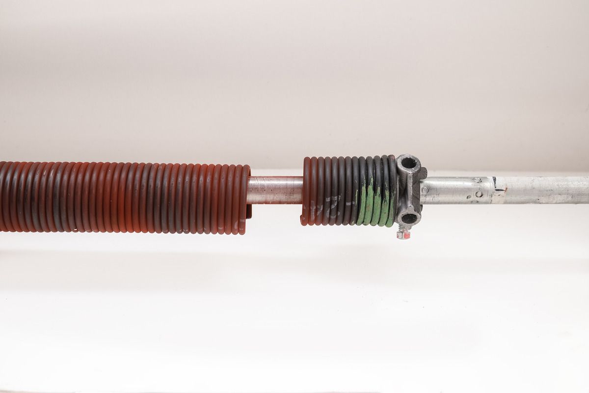 Close-up of a copper coil spring with a dark clamp attached to a clear tube on a white background