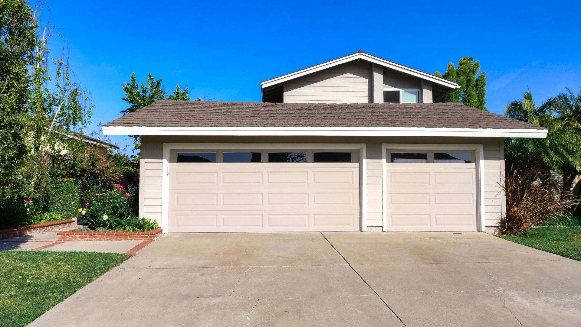 Suburban two-story house with a white garage and driveway under a blue sky