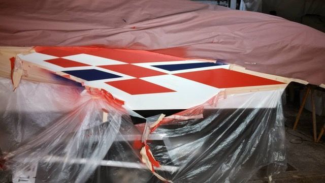 A white table holds a partially painted piece with red, white, and blue checkered pattern, covered in plastic.