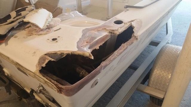 Damaged white boat hull with large section missing, exposing interior structure.