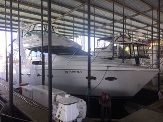 White yacht docked in a covered boat slip, under a metal roof, with other boats nearby.