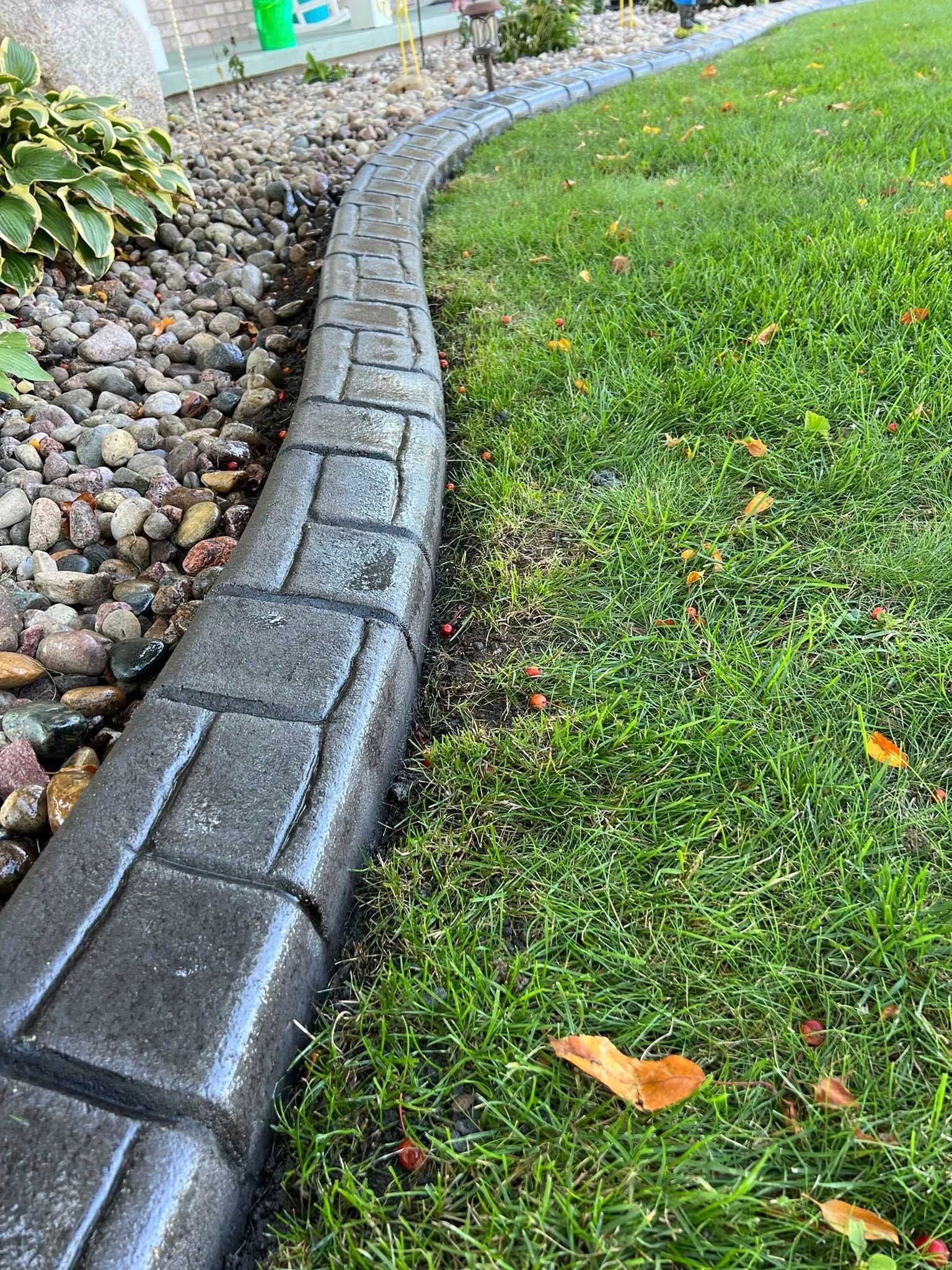Curved stone garden border between mulch rocks and green grass