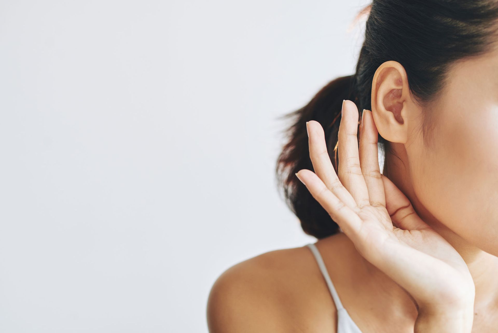 Close-up of a person cupping their ear, wearing a white strap, against a light background Close-up of a person cupping their ear, wearing a white strap, against a light background