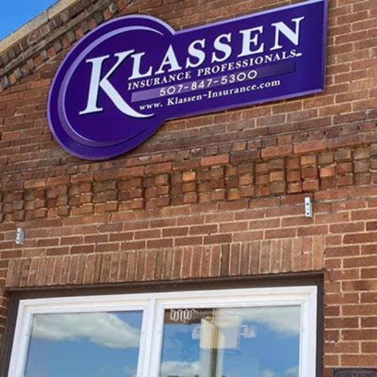 Klassen Insurance Professionals sign on a brick building with a white-trimmed window. Purple and white color scheme.