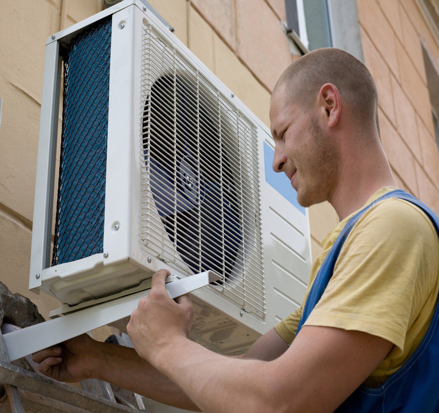 A man is fixing an air conditioner on the side of a building