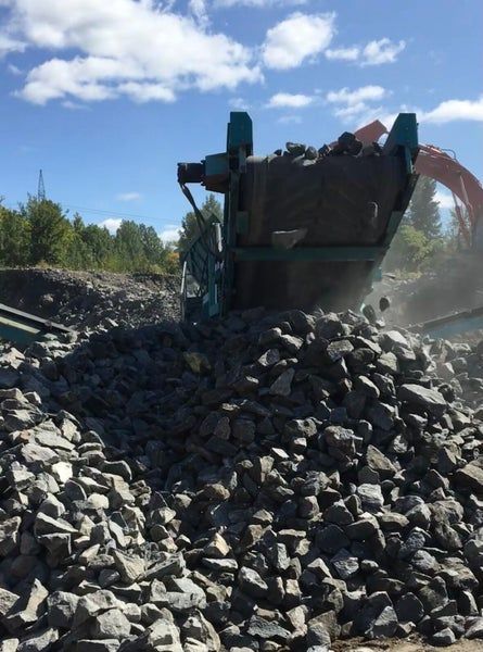 Sous un ciel radieux et ensoleillé, une imposante machine industrielle traite des roches grises dans une carrière.