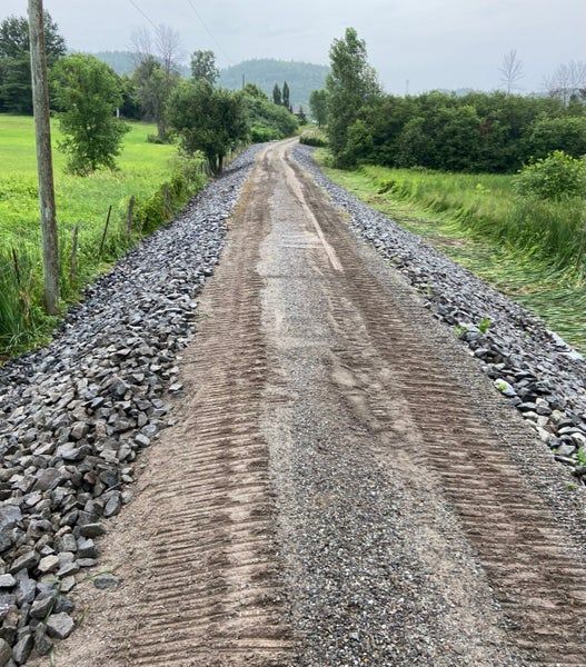 Un chemin de terre et de gravier traverse un paysage verdoyant, bordé de part et d'autre par de gros rochers sombres.