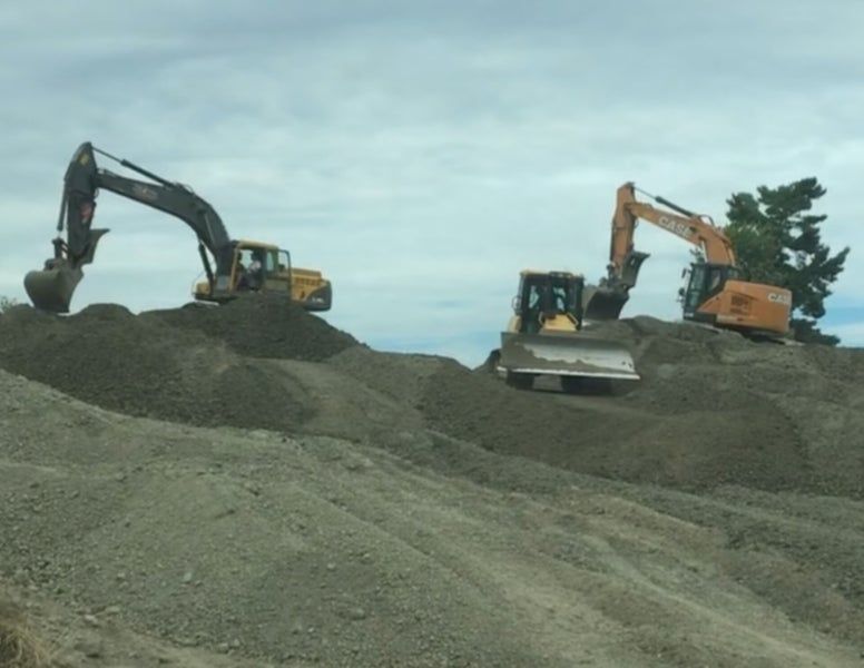 Deux excavatrices et un bulldozer étaient stationnés sur de grands tas de terre sous un ciel nuageux.