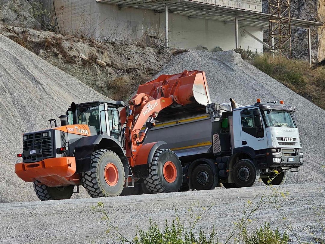 Una pala caricatrice arancione scarica ghiaia in un camion bianco in una cava.