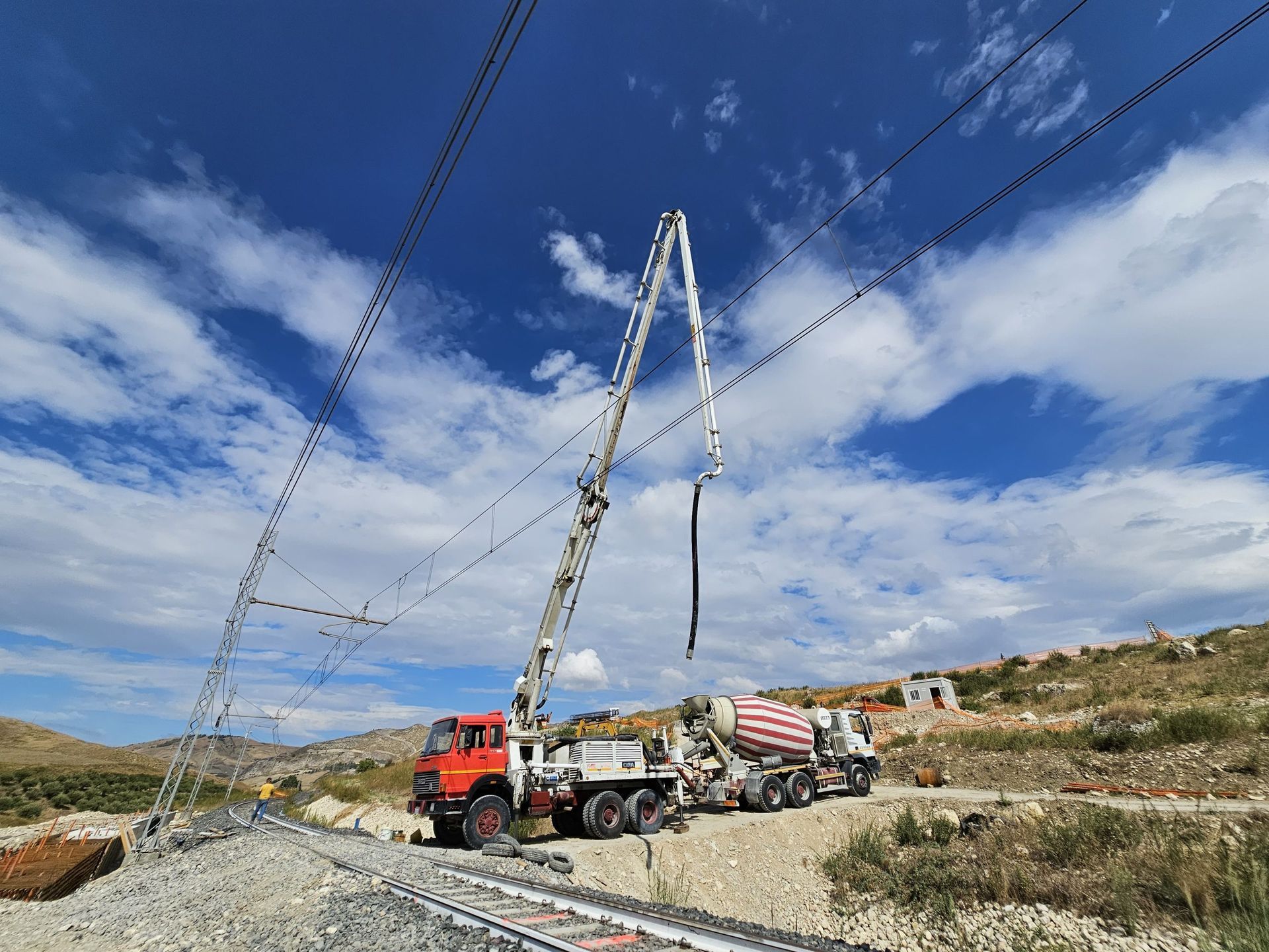Un camion di servizio che solleva i cavi elettrici in un campo rurale arido, sotto un cielo azzurro e parzialmente nuvoloso.