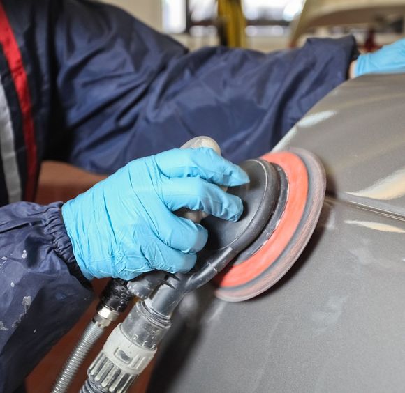 Mani guantate che usano uno strumento abrasivo su una superficie grigia di un'auto