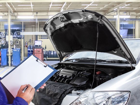 Meccanico che ispeziona il motore di un'auto in un'officina, con in mano un blocco appunti.