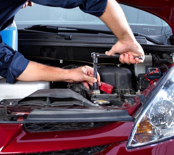 Persona che usa una chiave inglese per riparare il motore di un'auto sotto il cofano aperto.