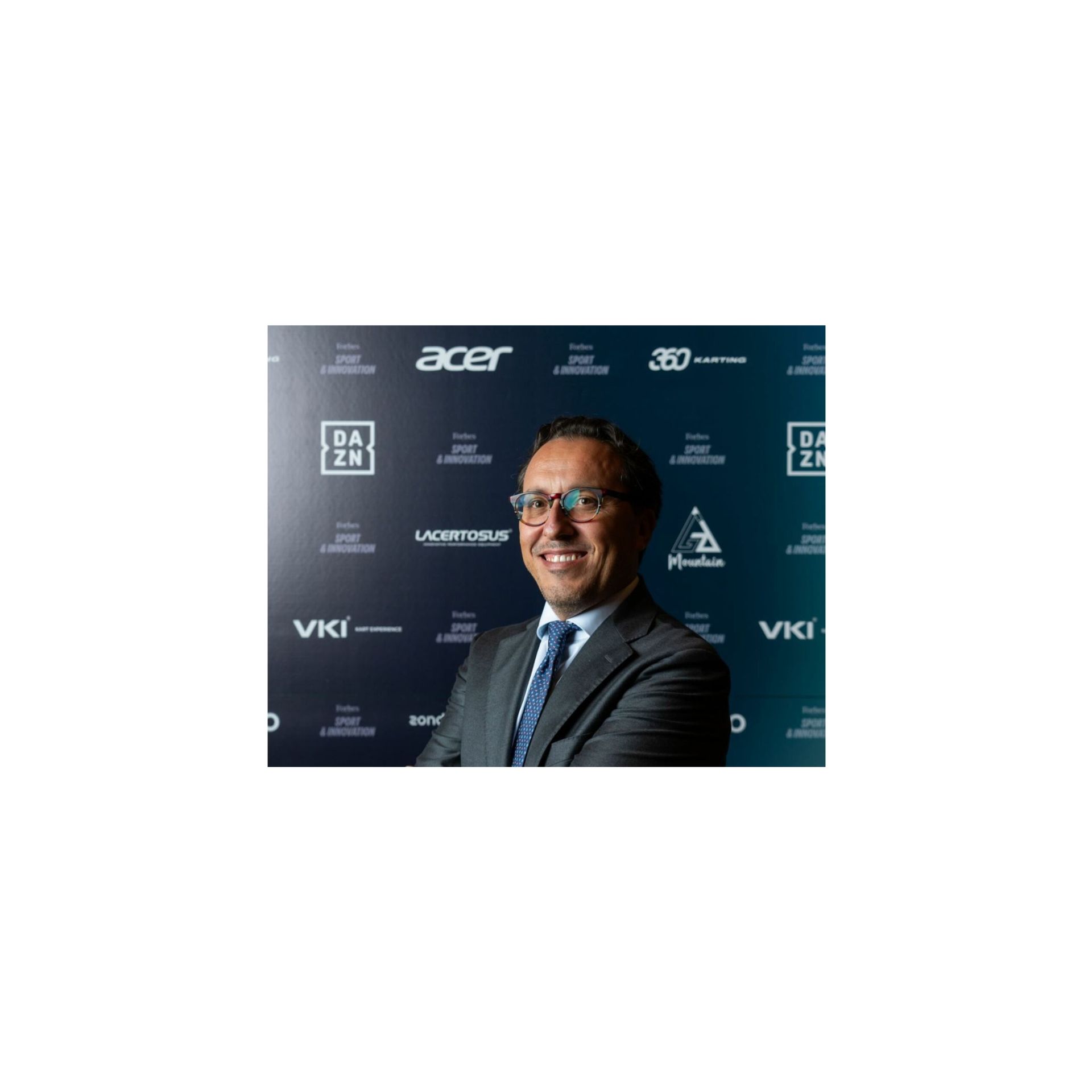 Man in suit smiles in front of a backdrop with logos.