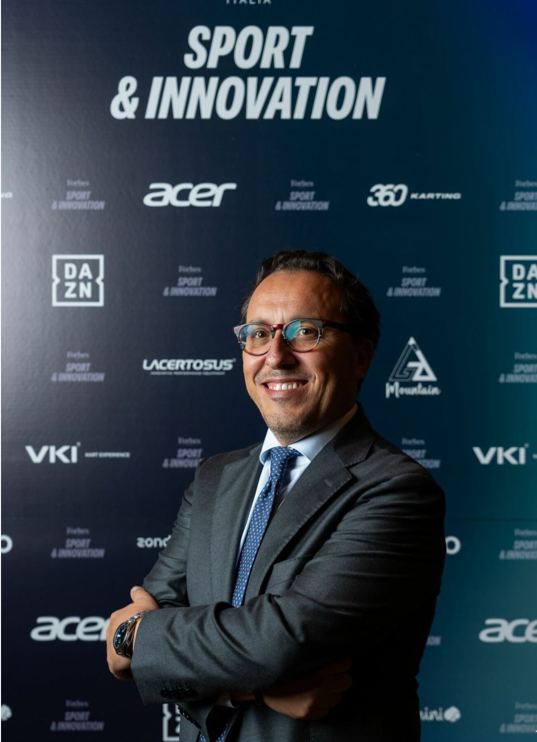 Man in suit smiles in front of a backdrop with logos.