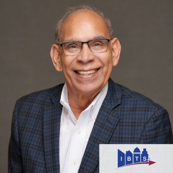 A man wearing glasses and a suit is smiling in front of an ibts logo