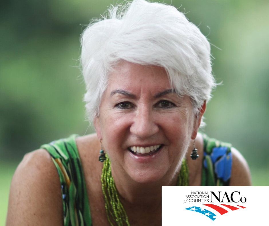 A woman with white hair is smiling in front of a naco logo