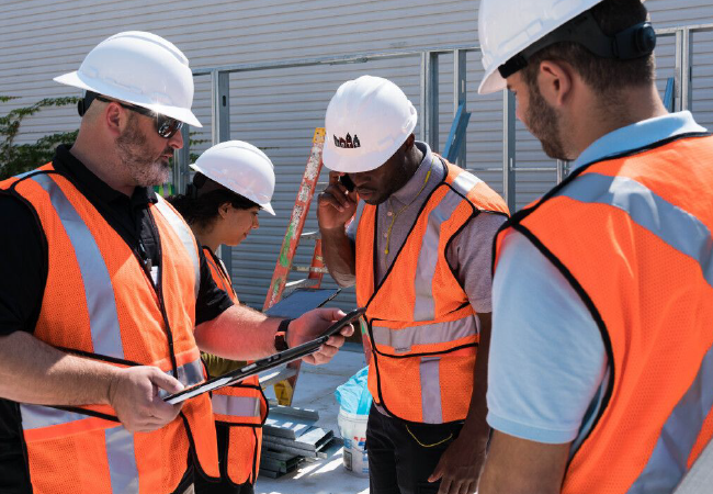 Trabajadores de la construcción con cascos y chalecos de seguridad revisan los planos en una tableta en un sitio de construcción.