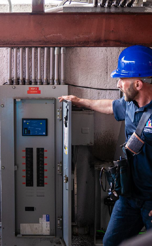 A man in a blue hard hat is standing next to a electrical box.