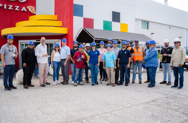Grupo de personas con cascos de seguridad afuera de un edificio con paneles de colores, posiblemente un sitio de proyecto de construcción.