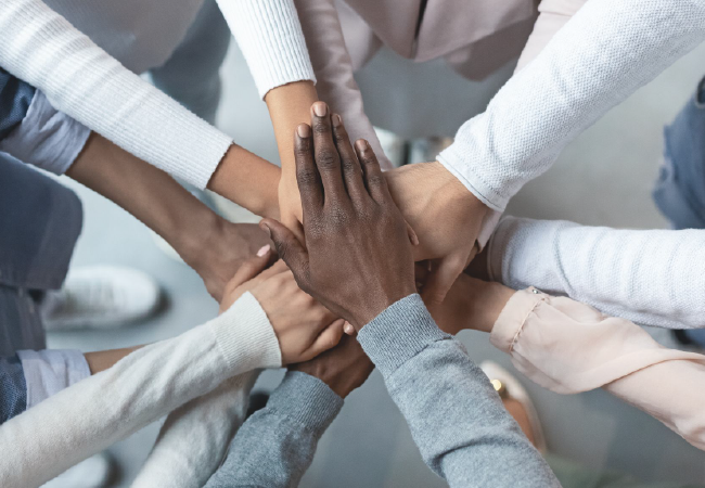 Manos de diversas personas unidas en una pila, simbolizando el trabajo en equipo y la unidad.