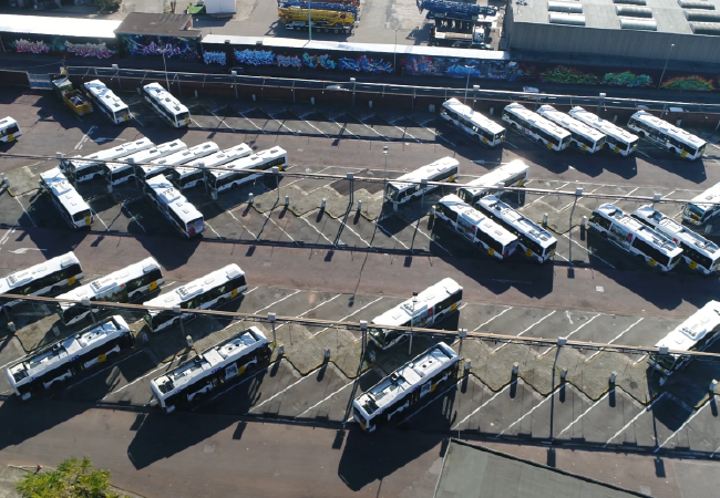 Vista aérea de una estación de autobuses llena de autobuses estacionados, dispuestos en espacios de estacionamiento en ángulo.
