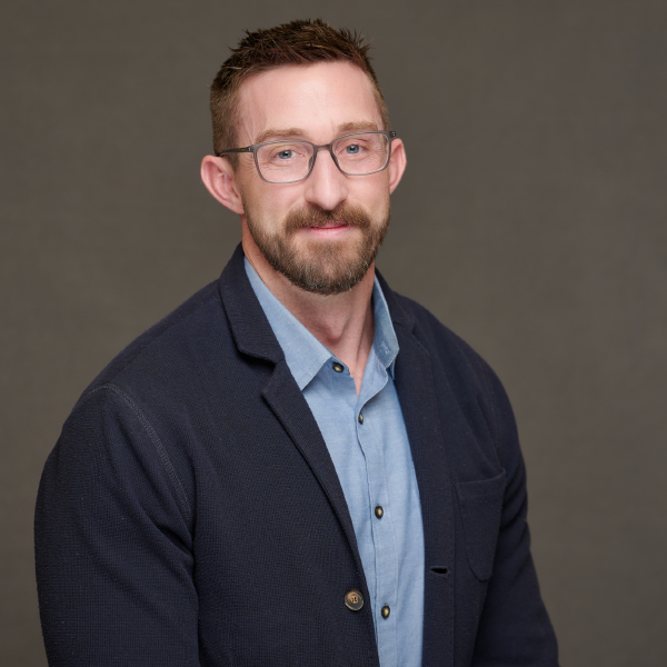 A man with a beard and glasses is wearing a blue jacket and a blue shirt.