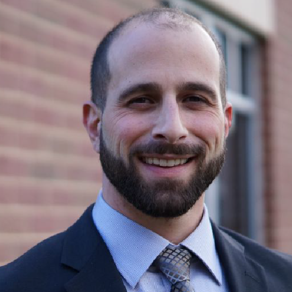 A man with a beard wearing a suit and tie is smiling