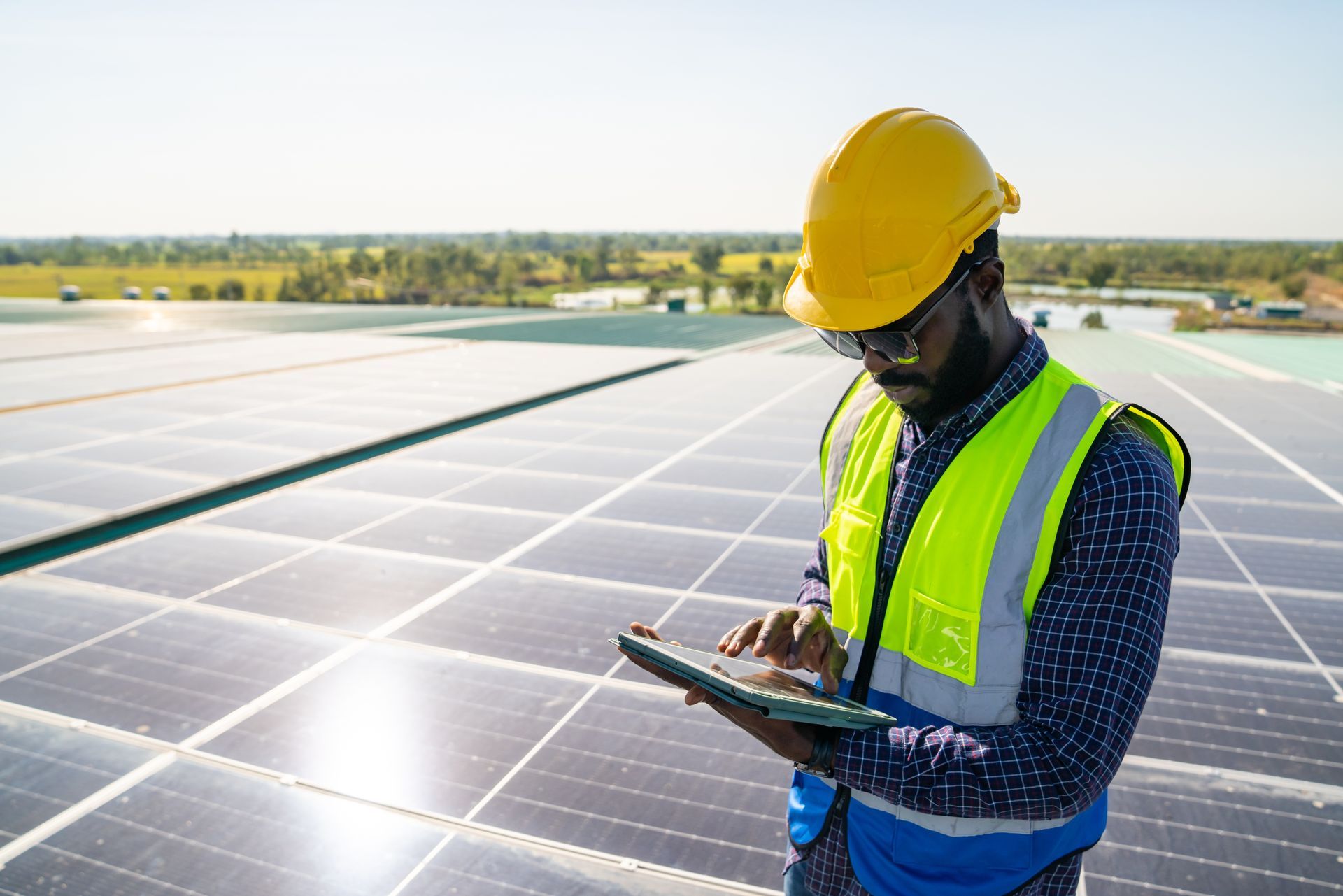 A man is standing on top of a solar panel looking at a tablet.