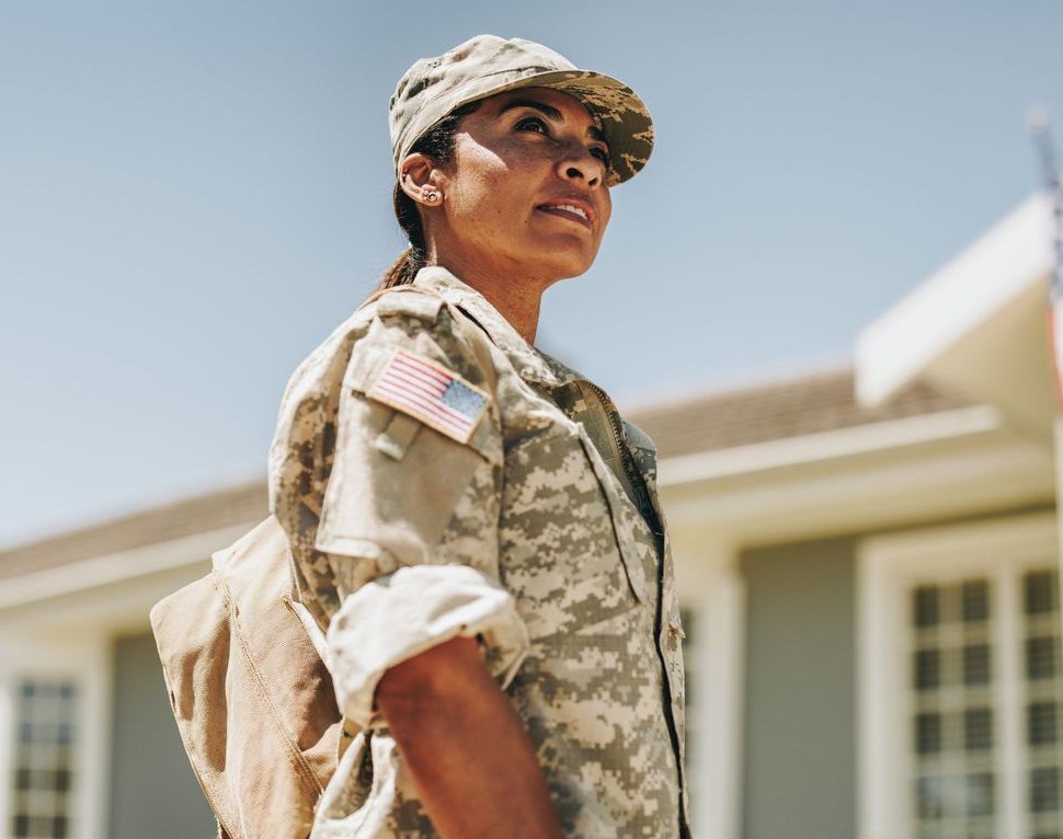 A woman in a military uniform is standing in front of a house.