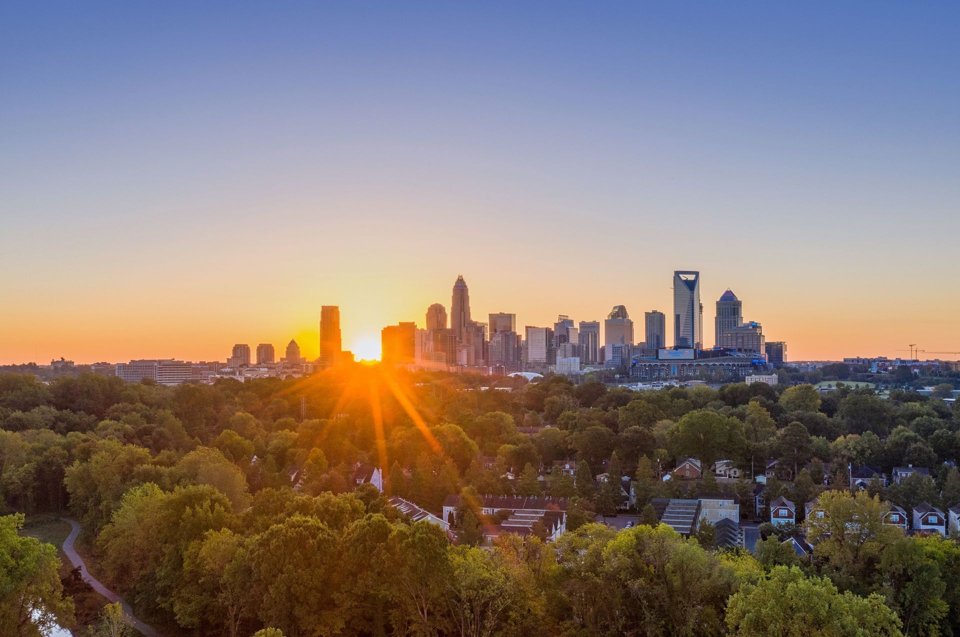 An aerial view of a city skyline at sunset with the sun shining through the trees.