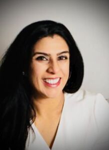 A woman with long black hair is smiling and wearing a white shirt.