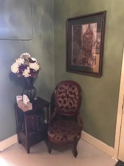 Corner with chair, side table, artwork, and flowers. Green and brown tones.