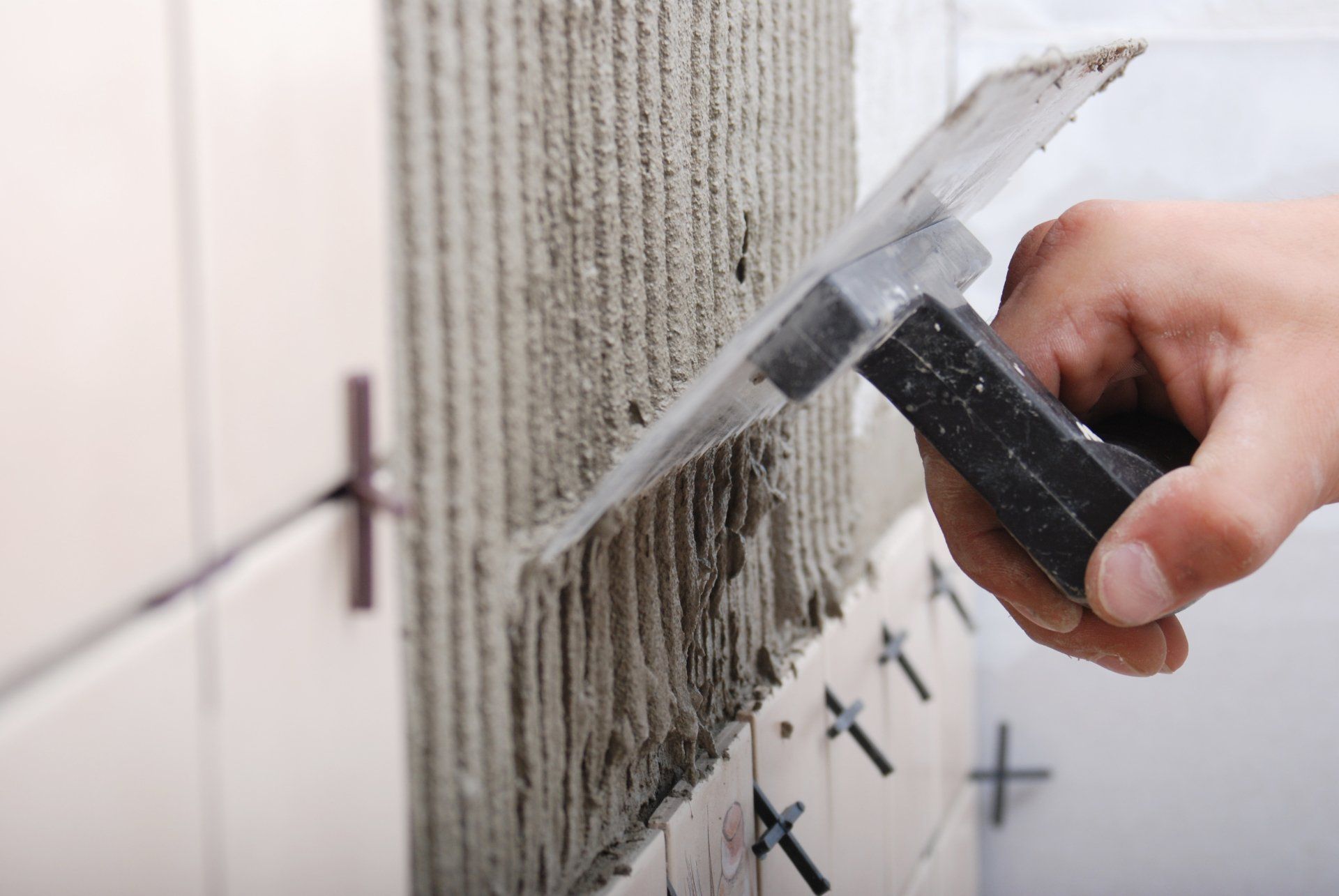 Una persona sta applicando le piastrelle a un muro con una cazzuola.