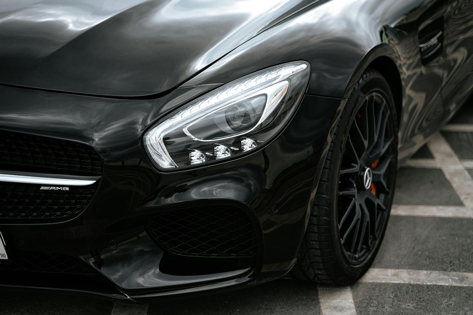 Close-up of the front headlight and wheel of a sleek black Mercedes-Benz sports car parked on paved ground.