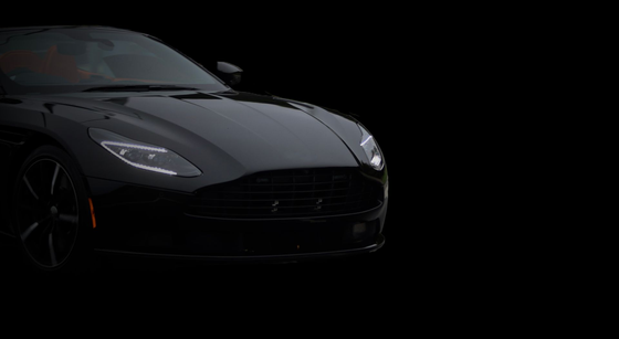 A sleek, black Aston Martin sports car captured from the front quarter against a solid black background.