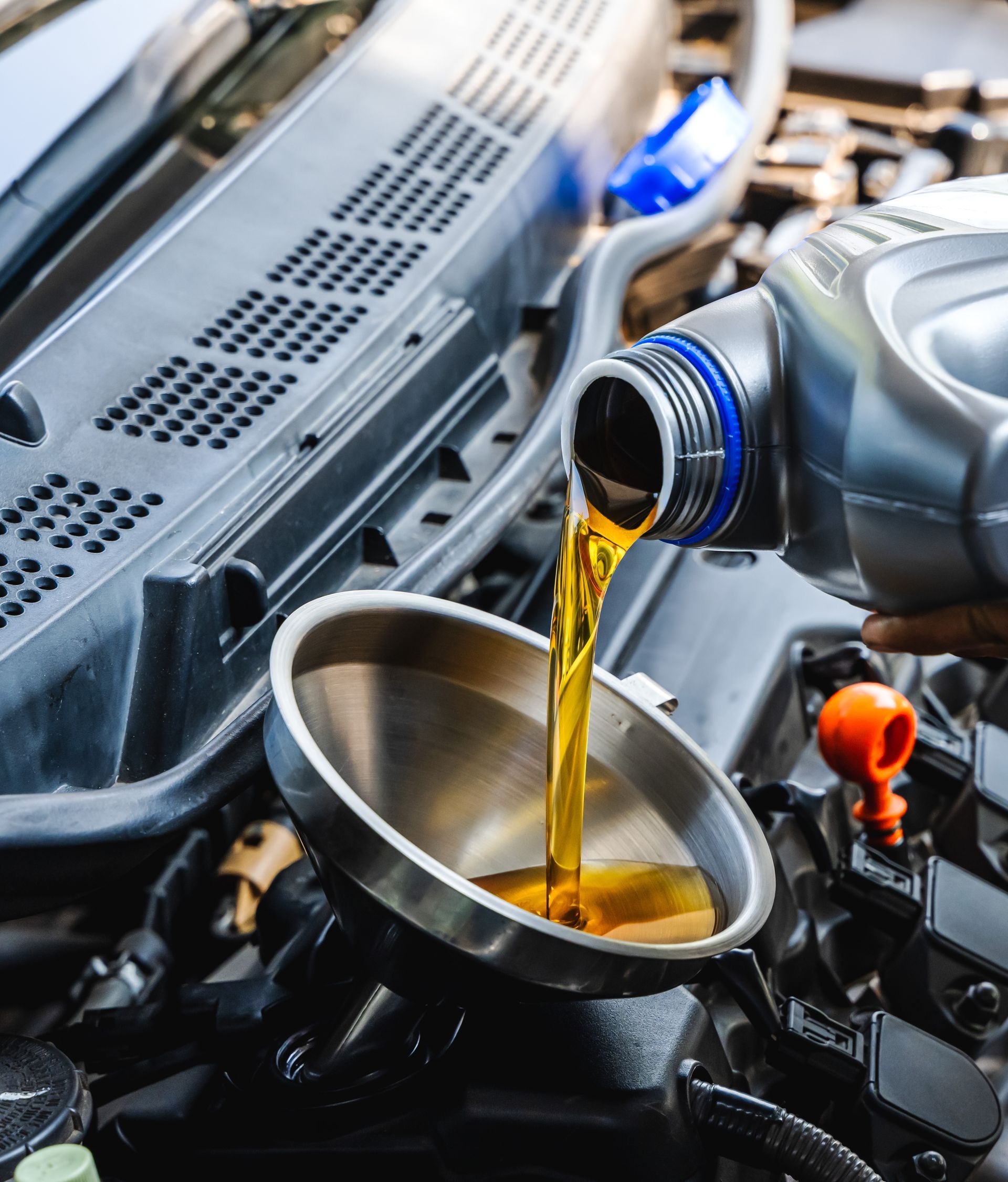 Golden motor oil being poured from a plastic container into a metal funnel placed in a car engine.
