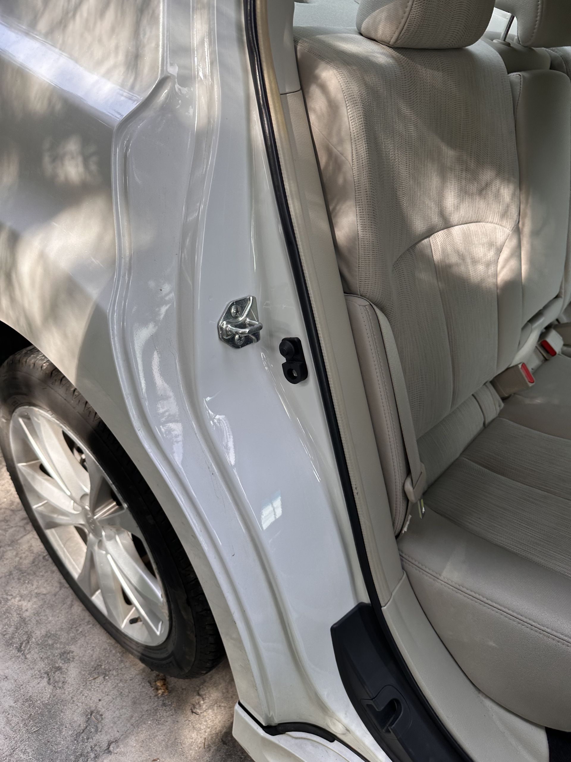 White car door ajar, showing interior. Beige seat, black door latch, silver wheel.