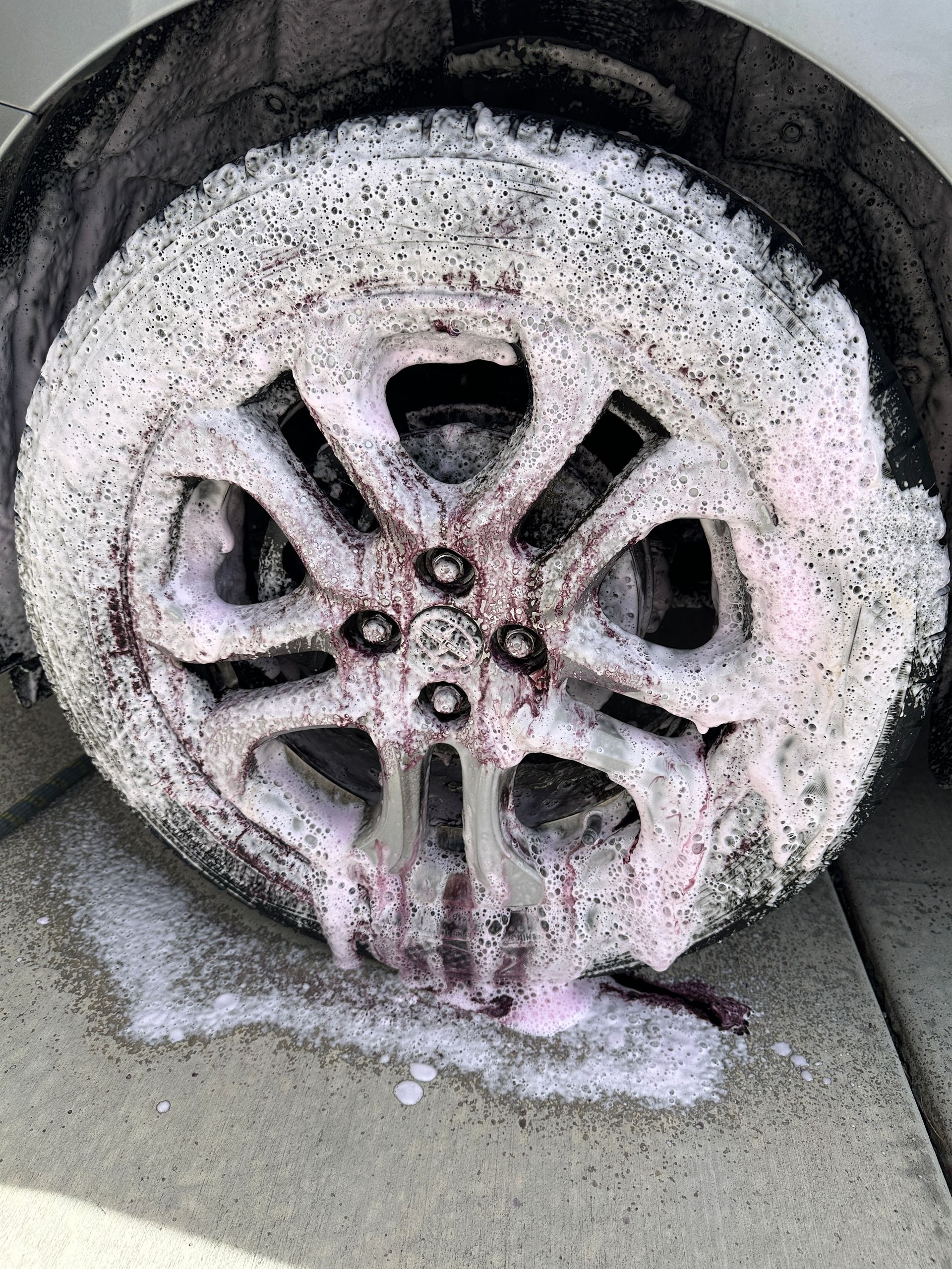 Car wheel covered in pink foam, on a concrete surface.